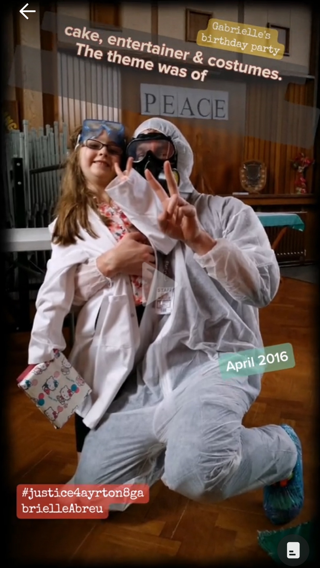 April 2016, photo of Gabrielle Abreu & daddy holding 2 fingers up as peace sign, with both of them wearing lab coat or hazmat suit, as part of Gabrielle's birthday party theme of a science lab, during its celebration in a church hall in Grimsby. Click to watch full clip