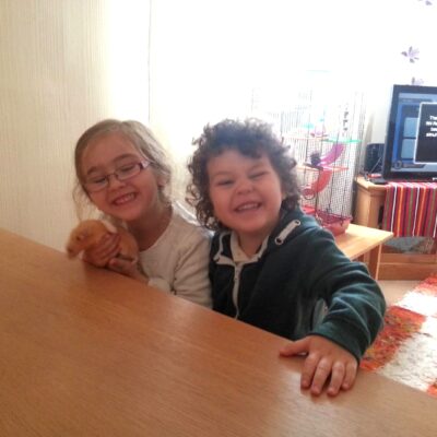 May 2015, photo of Ayrton & Gabrielle Abreu smiling whilst sat at the dinning table in the living room. This photo is part of a group that will help provide some perspective to layout & dimensions for their living room. This photo is from a side wall & faces the front wall of the living room. Click on it to expand.